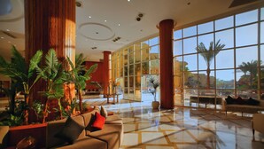 A spacious lobby with a large seating area, a glass wall offering a view of the outside, and a variety of indoor plants. - Eagles Downtown Zahabia Aqua Park (Hurghada)