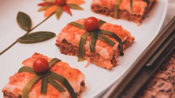 Une assiette rectangulaire blanche contenant trois portions de nourriture, décorées de feuilles vertes et de baies rouges, est posée sur un comptoir en granit.