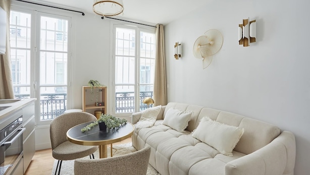 A modern living room with a beige sofa, a round table with chairs, a bookshelf, and a large window with curtains. - Cosy and New Studio Center of Paris (Paris)