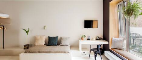 Quarto moderno com cama, escrivaninha e um assento junto à janela.