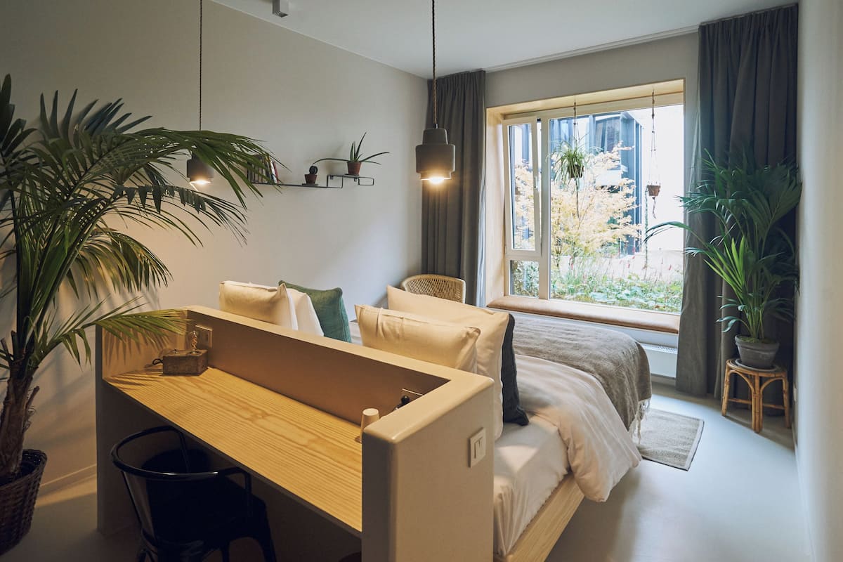 A modern bedroom with a bed, a desk, and a window with curtains.