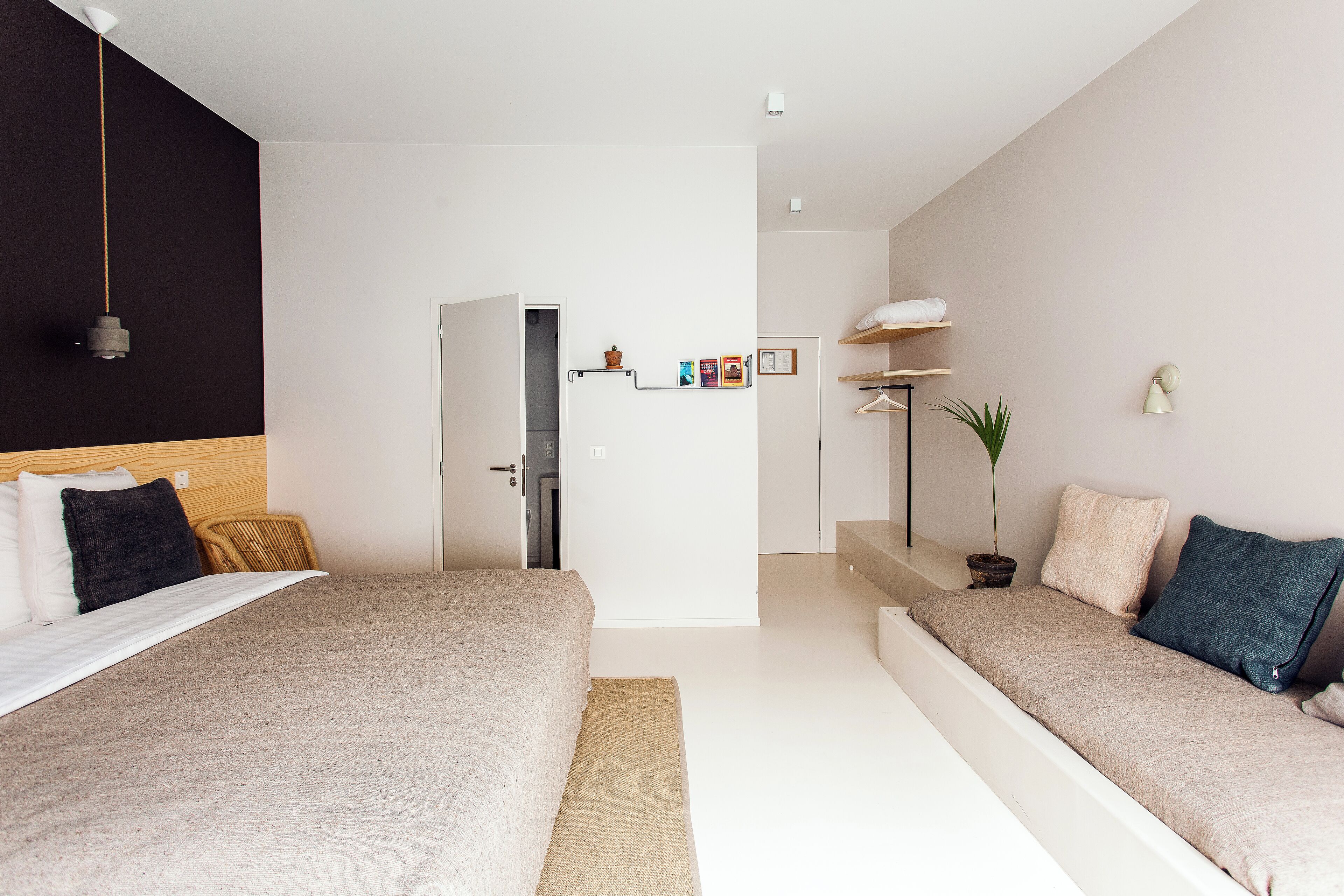 A modern hotel room with two beds, a large window, a flat-screen TV, and a small kitchenette.