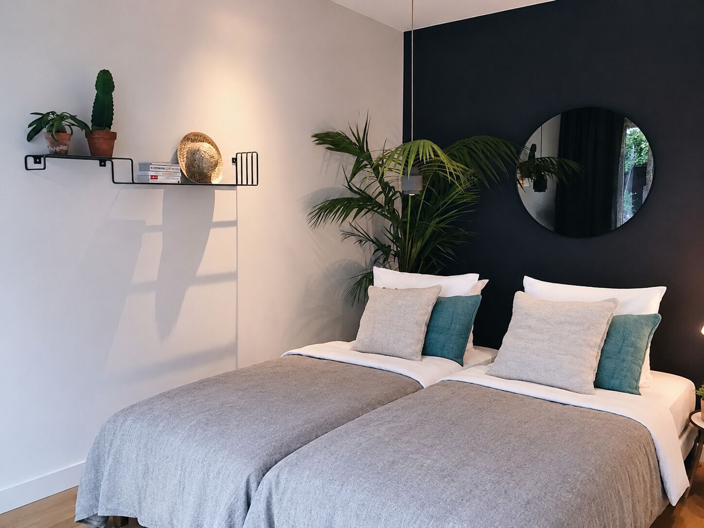 Ein modernes Schlafzimmer mit einem Bett, Zimmerpflanzen, einem Wandspiegel und einem Regal mit Dekoration.