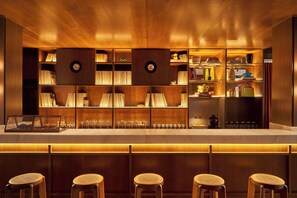A bar area with wooden shelves, bar stools, and a display case with glasses. - Latroupe Hotel Jardin Secret (Brussels)