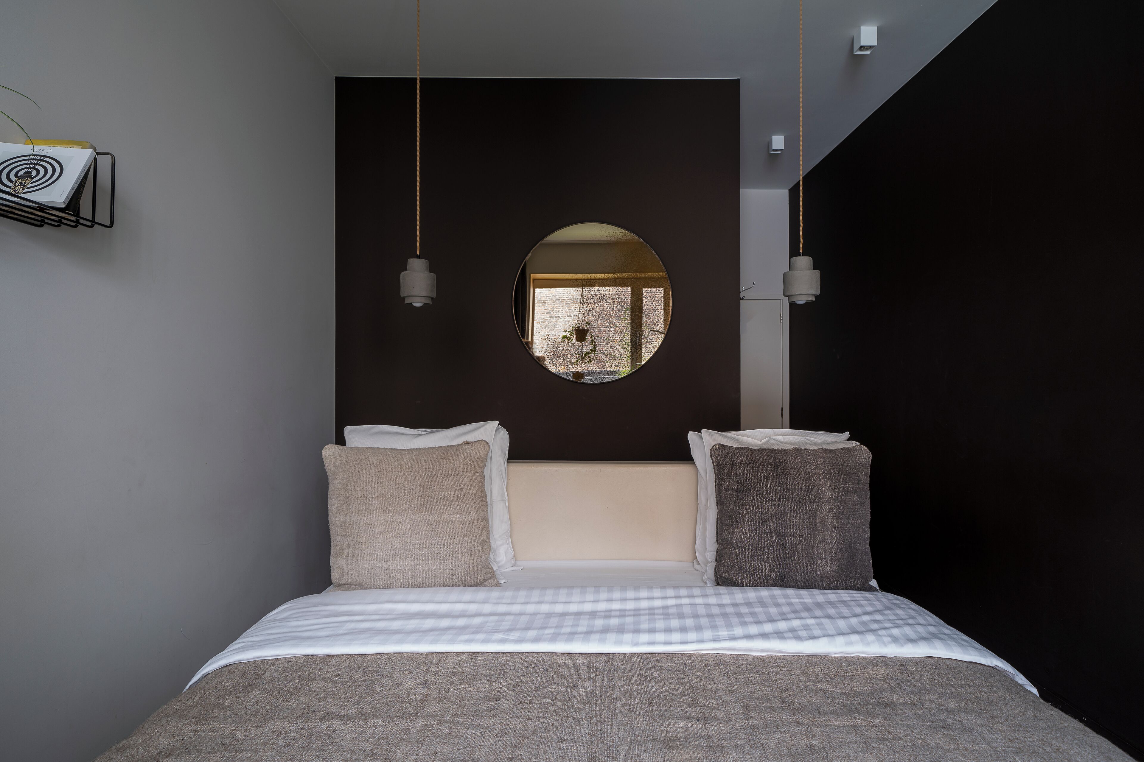 Une chambre à coucher moderne avec un grand lit, un grand miroir rond au mur et deux lampes suspendues.