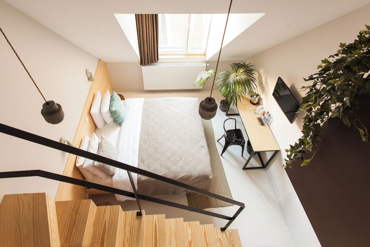 A modern loft bedroom with a skylight, a bed, a desk, and a staircase.