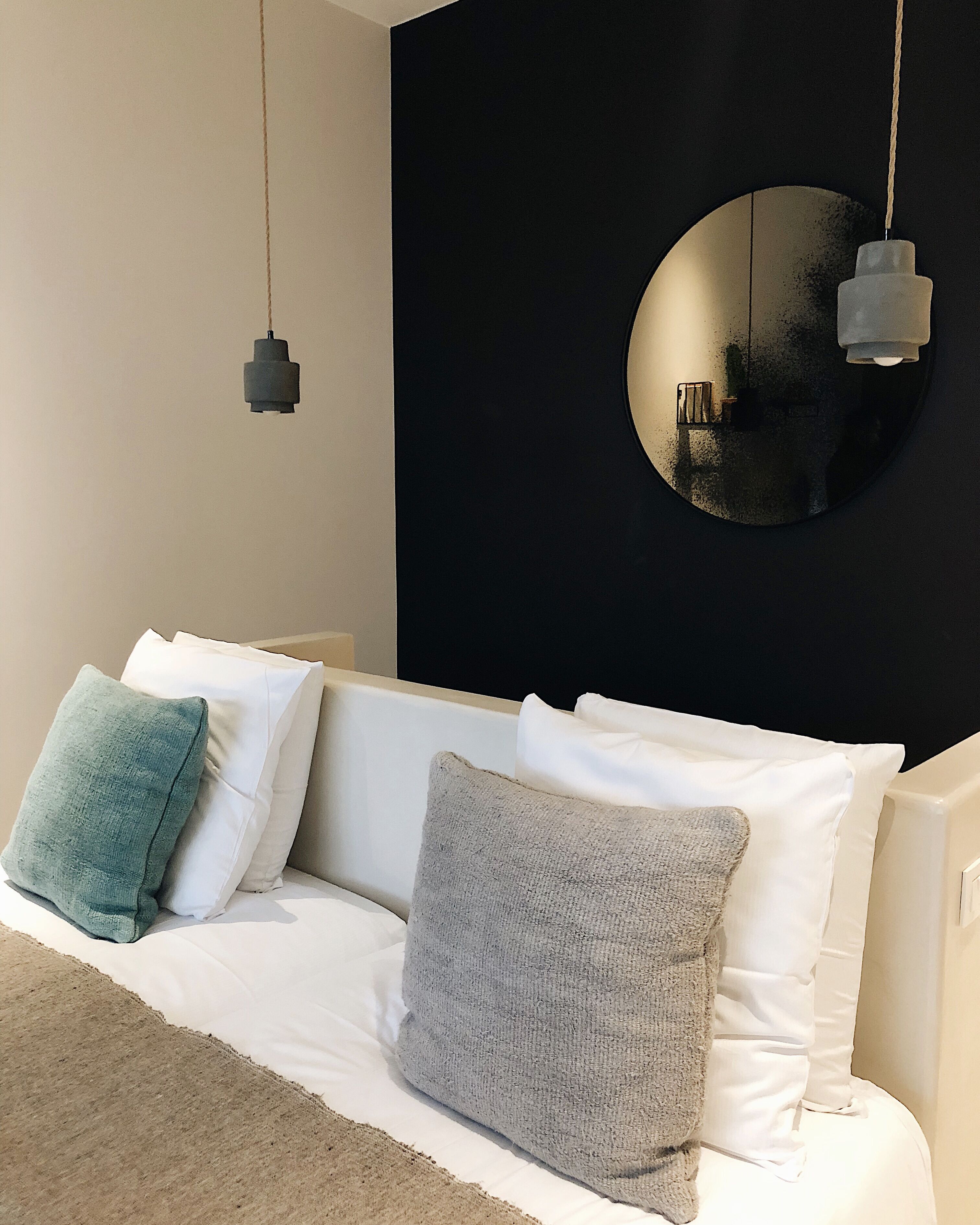 A modern bedroom with a white sofa, two pillows, a round mirror, and two hanging lights.