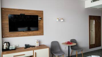 Habitación de hotel con un escritorio de madera, un televisor montado en la pared, una mesita redonda con dos sillas, un minibar y una puerta con espejo.