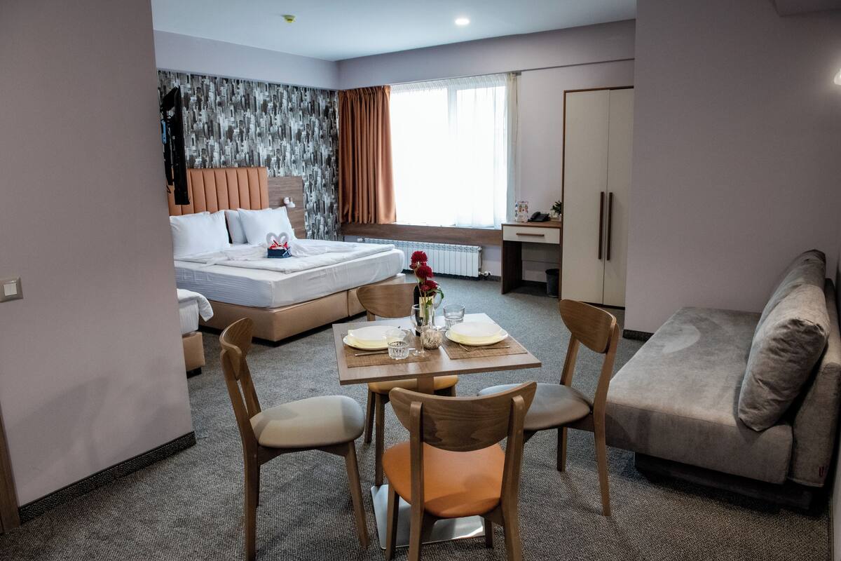A hotel room with a bed, a dining table with chairs, a sofa, and a desk.