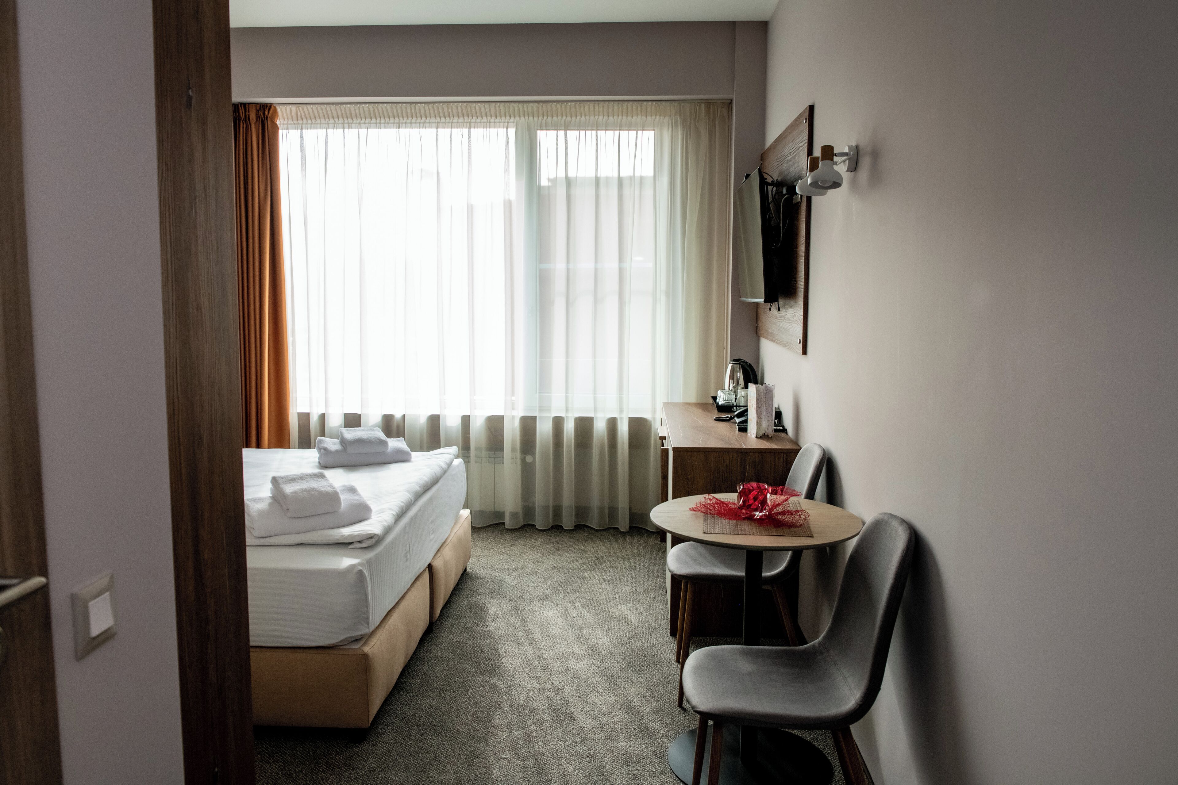 Habitación de hotel con cama, escritorio, silla y ventana con cortinas.