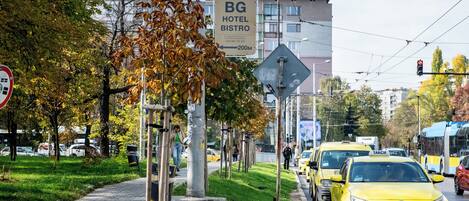 A street with a BG Hotel Bistro sign, yellow taxis, and a pedestrian crossing.
