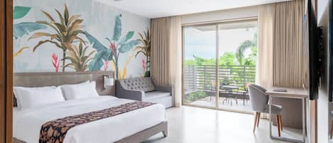 Habitación de hotel con una cama grande, un escritorio y un balcón con vistas a zonas verdes.