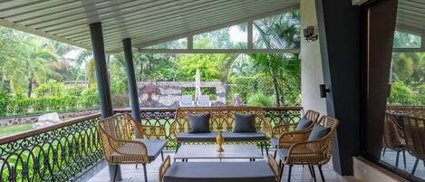 An outdoor patio with wicker furniture, a table, and a view of lush greenery.