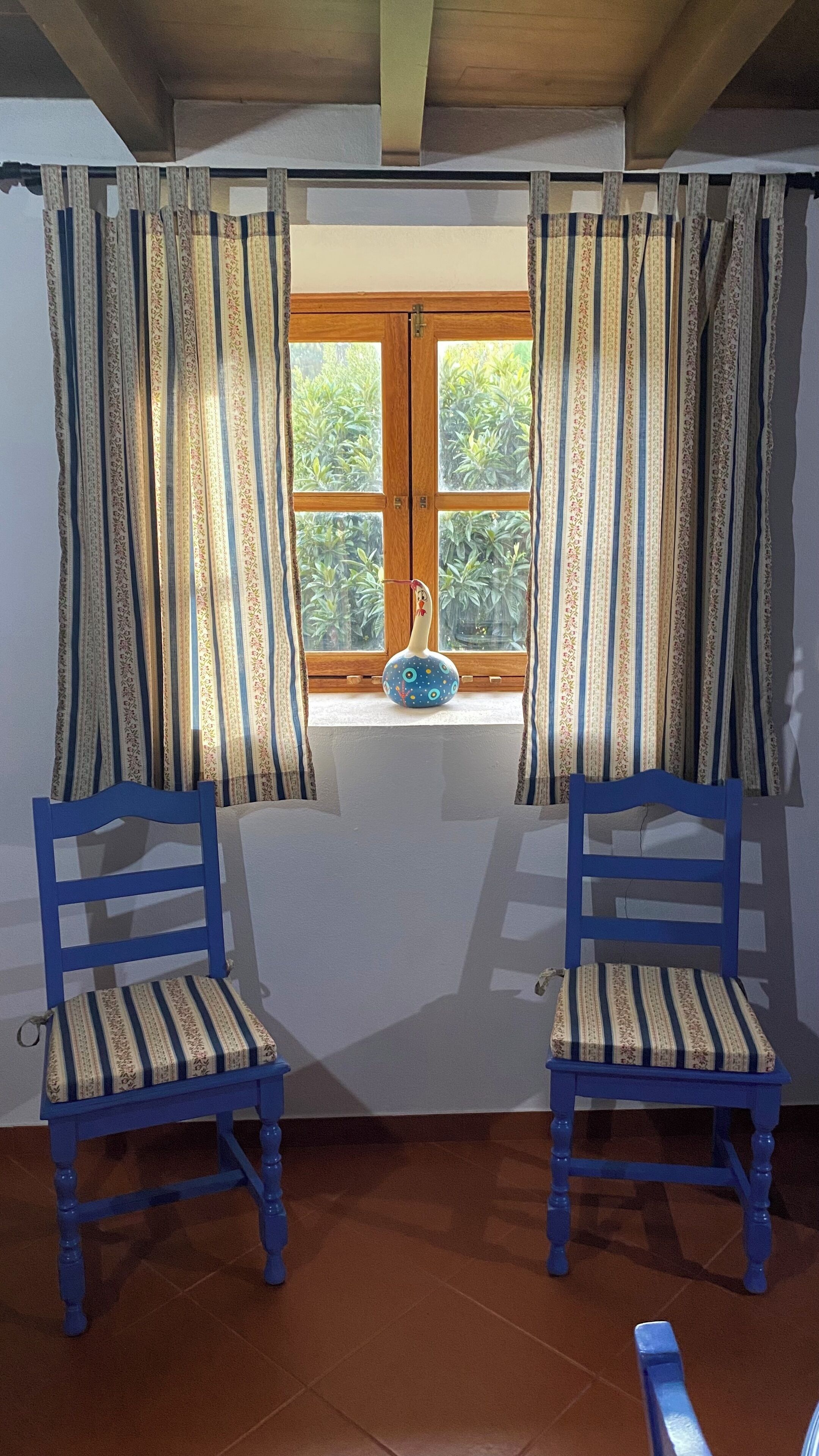 Een kamer met twee blauwe stoelen, een raam met gordijnen en een vaas op de vensterbank.