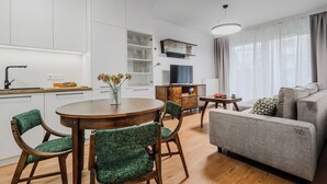 A modern kitchen with white cabinets, a dining table with chairs, a sofa, and a TV.