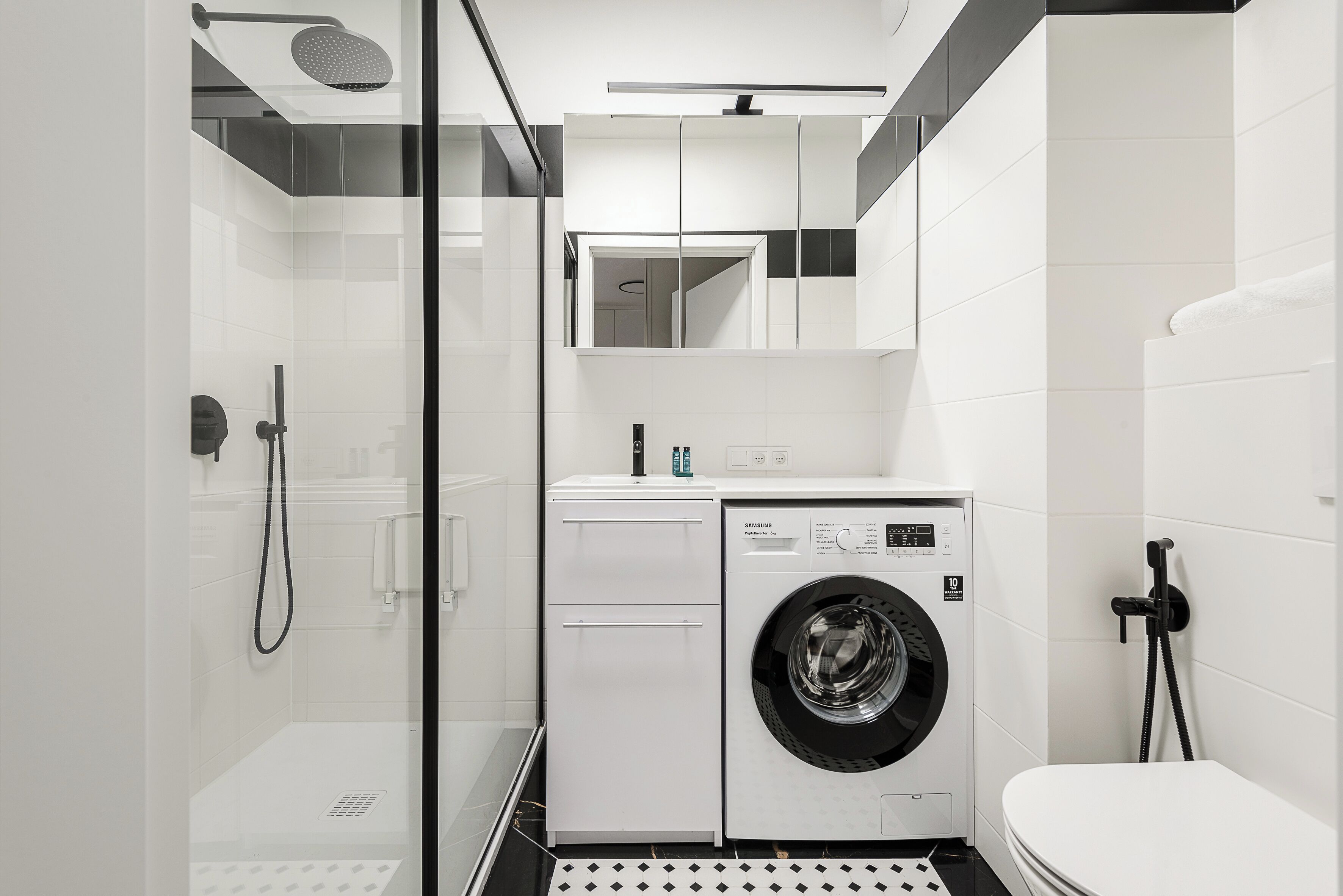 Une salle de bain moderne avec une douche à parois de verre, un lave-linge encastré et des toilettes.