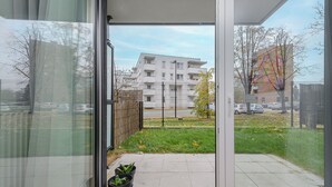 A view from a balcony with a metal fence, a grassy area, and a building in the background.