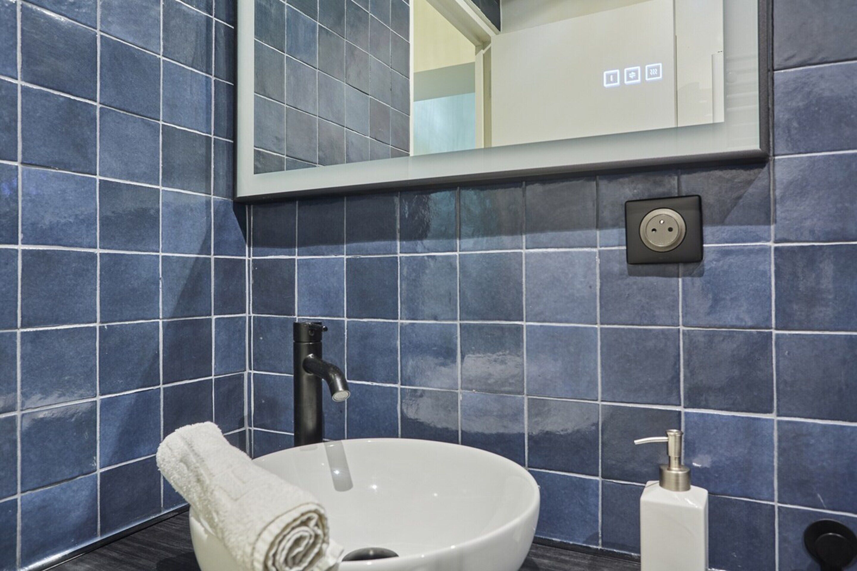 Ein Badezimmer mit einem weißen Waschbecken, einem schwarzen Wasserhahn und einem auf der Ablage gerollten Handtuch.