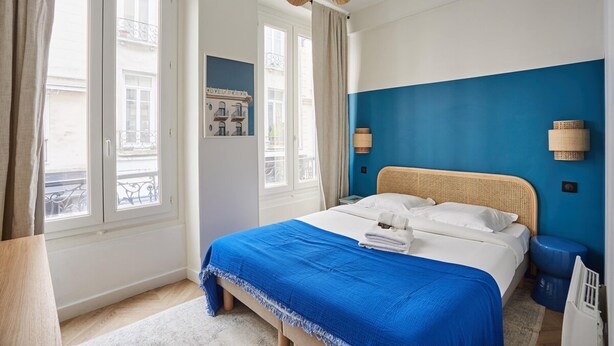 A bedroom with a bed, a window, a wall-mounted lamp, and a view of the outside. - Charming & Modern Duplex Apartment Center of Paris (Paris)