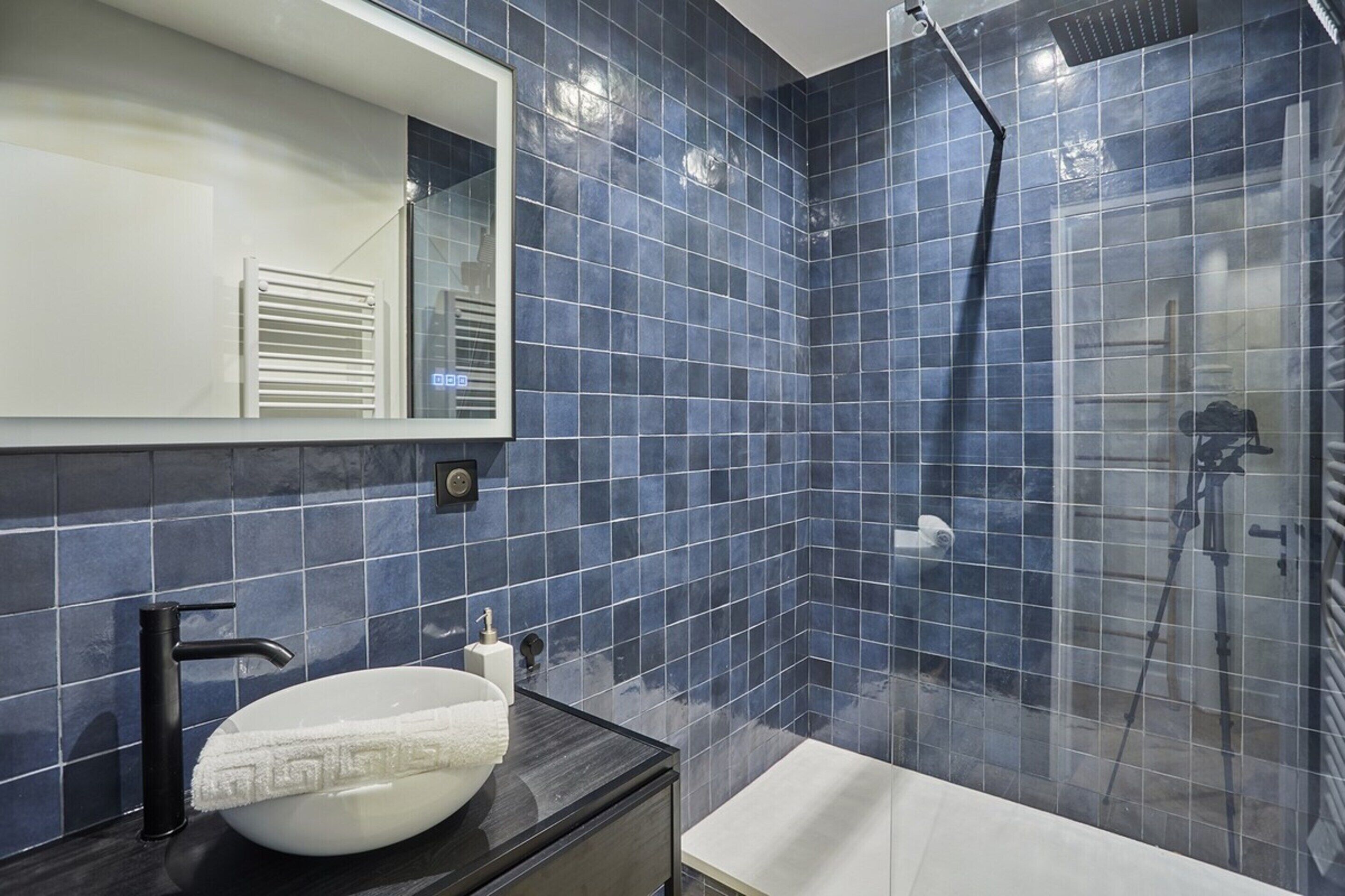 Une salle de bain moderne avec un lavabo blanc, un plan de toilette foncé et un grand miroir.