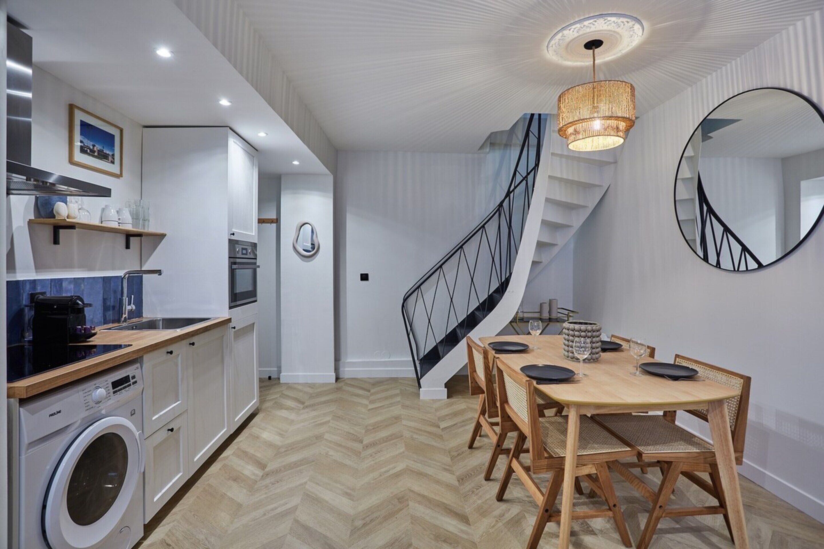 Eine moderne Küche mit integriertem Waschmaschine, ein Essbereich mit Holztisch und Stühlen sowie eine Wendeltreppe.