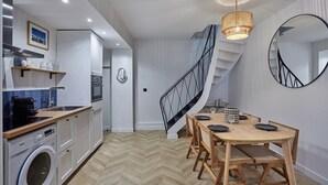 A modern kitchen with a built-in washing machine, a dining area with a wooden table and chairs, and a spiral staircase. - Charming & Modern Duplex Apartment Center of Paris (Paris)