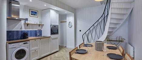 Una cocina moderna con lavadora integrada, un comedor con mesa y sillas de madera, y una escalera de caracol.