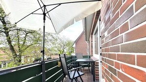 A balcony with a table and chairs, a white umbrella, and a brick wall.