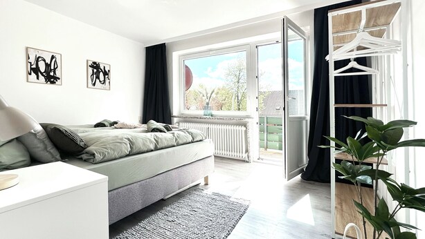 A modern bedroom with a bed, bedside table, and a view of the outdoors.