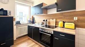 A modern kitchen with black cabinets, a built-in oven, a microwave, and a yellow kettle.