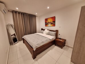 Een slaapkamer met een groot bed, een nachtkastje met een lamp, een spiegel en een schilderij aan de muur.