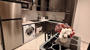 A modern kitchen with stainless steel appliances, a built-in oven, and a dishwasher. There is a dining table with chairs and a vase of flowers. - Loxwood House (Accra)