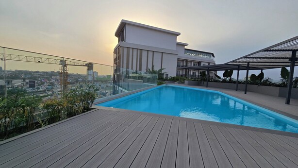 A rooftop pool with a wooden deck, surrounded by a glass railing and potted plants. - Loxwood House (Accra)