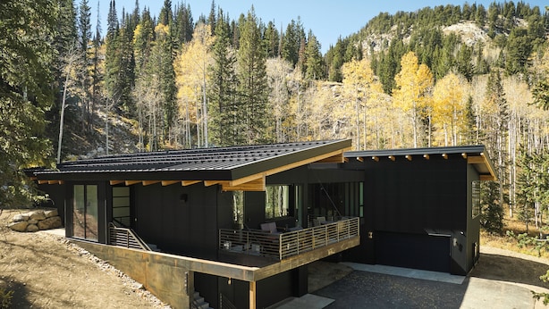 A modern cabin with a flat roof, large windows, and a balcony overlooking a forested area.