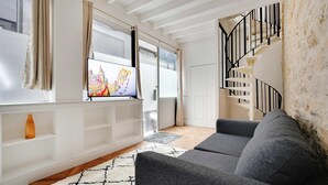 A modern living room with a grey sofa, a white entertainment unit, and a staircase with black railings. - Welcoming Apartment - 2br/8p - Bonne-nouvelle (Paris)