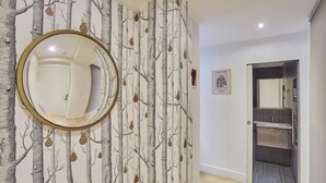 Ein Flur mit einem Wandspiegel, einer zur Toilette führenden Tür und einem gerahmten Bild an der Wand.
