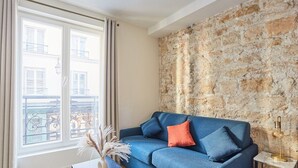 Ein Wohnzimmer mit einem blauen Sofa, einem kleinen Tisch mit einer Vase und einer Steinwand.