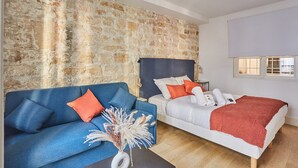 Ein Zimmer mit Steinwand, einem blauen Sofa, einem weißen Bett und einem Fenster mit Jalousien.