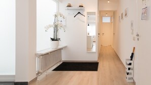 A modern hallway with a radiator, a black rug, a potted orchid, and a hat on a shelf. - Apartment in Ostend Near the Beach (Ostend)