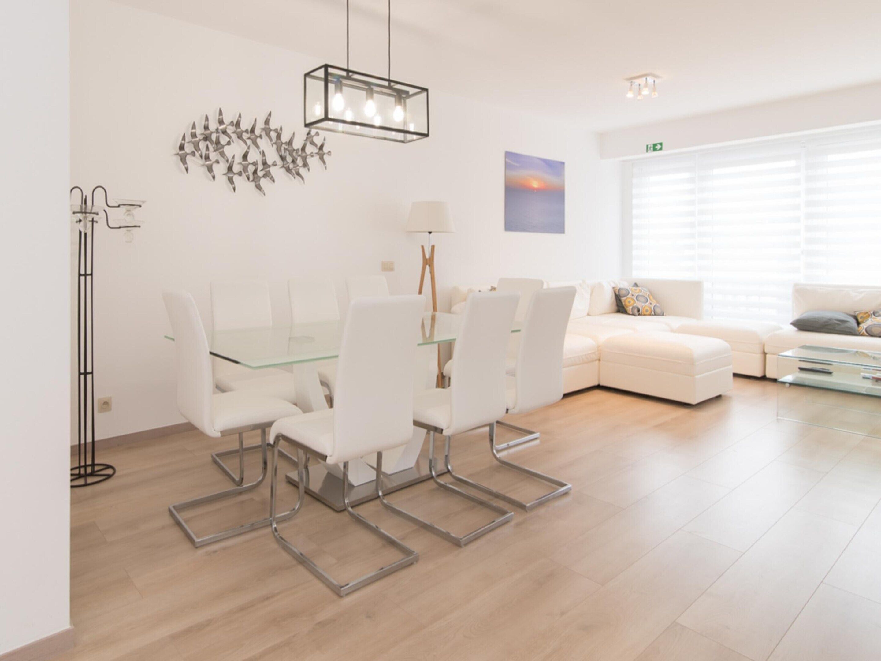 Ein modernes Wohnzimmer mit einem Glastisch, weißen Stühlen, einer Couch und einem Couchtisch.