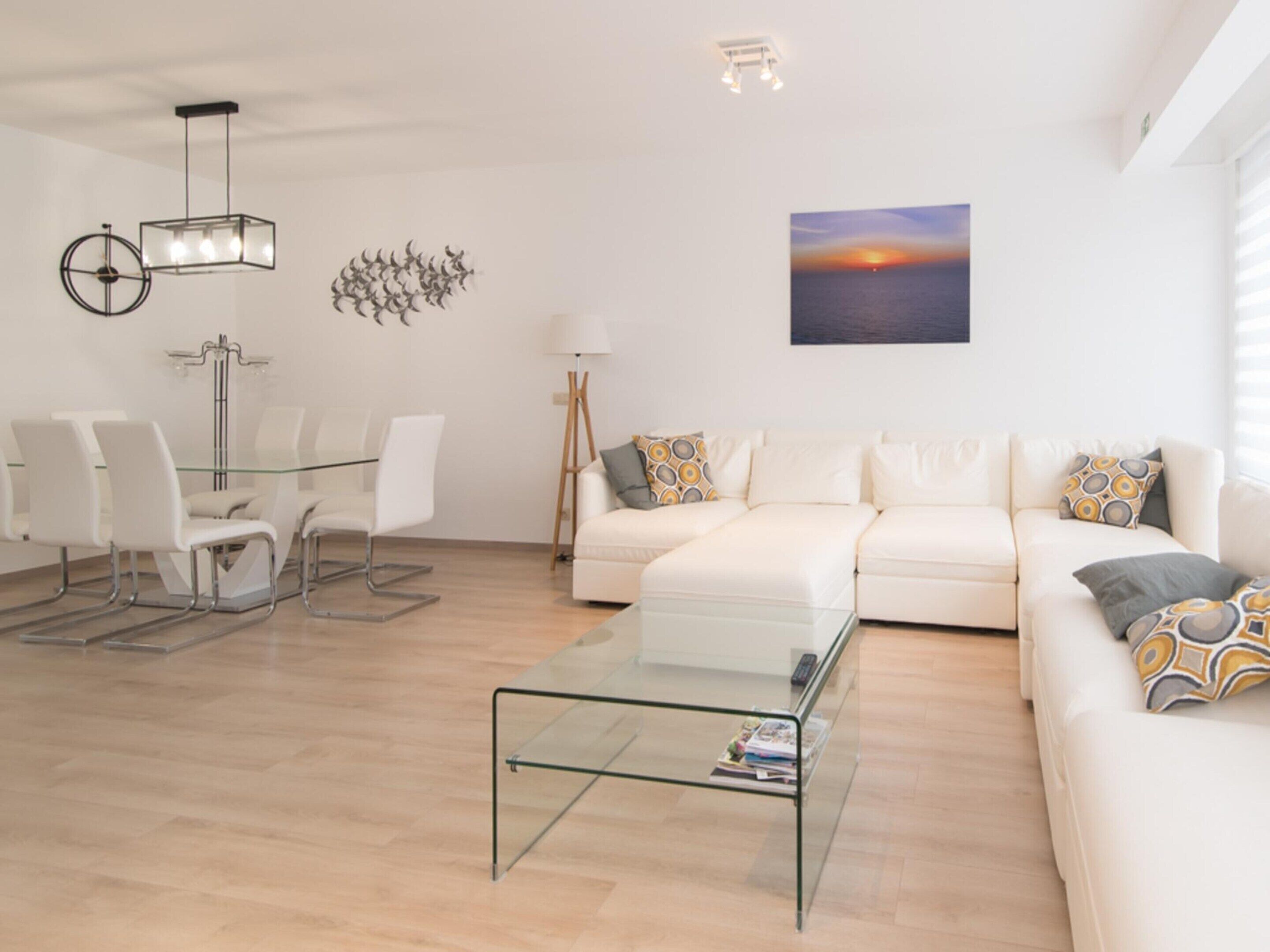 Un salon moderne avec une table basse en verre, des canapés blancs et un coin repas comprenant des chaises et une table en verre.