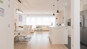 A modern kitchen with a central island, a dining area with a glass table, and a living space with a sofa and a TV. - Apartment in Ostend Near the Beach (Ostend)