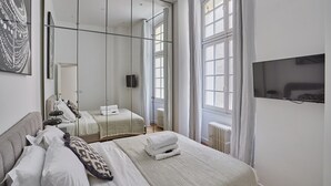 Ein modernes Schlafzimmer mit einem großen Bett, einem Kleiderschrank, einem Fernseher und einem Fenster mit Vorhängen.