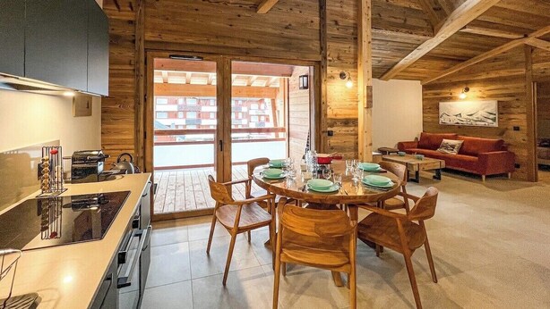 A cozy cabin interior with a wooden dining area, a kitchen with modern appliances, and a living space with a red sofa.