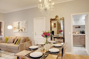 A dining area with a table set for four, a chandelier, a mirror, and a sofa with patterned cushions. - Paris Blanc Manteau Residence (Paris)