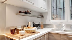 A modern kitchen with a built-in oven, a coffee maker, and a toaster. There are wooden cabinets and a countertop with a basket of croissants.