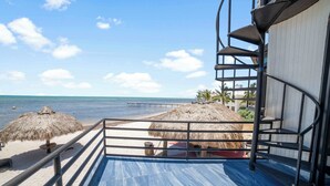 A balcony with a view of the beach, a thatched umbrella, and a staircase leading to an upper level. - Beach View Room Dormitory Room Barnacle Resort (Big Pine Key)