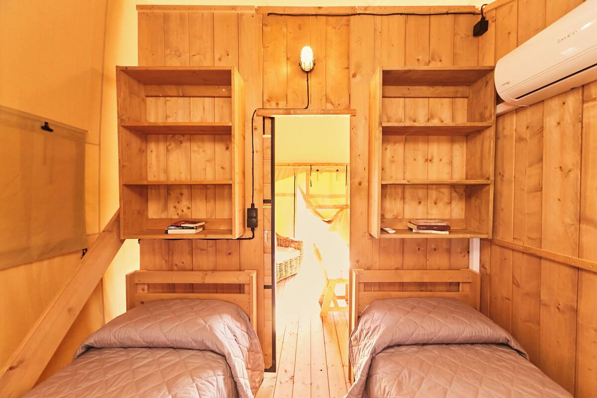 Une pièce en bois avec deux lits, des étagères intégrées et une échelle menant à un niveau supérieur.
