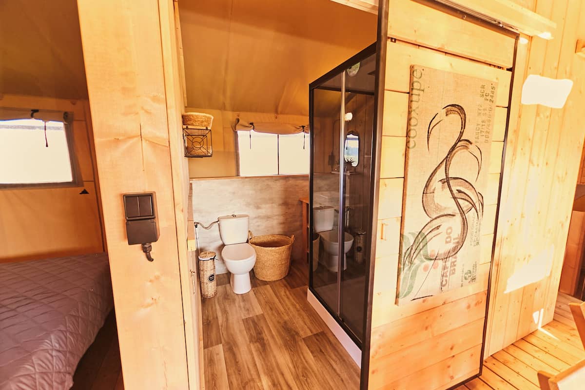 Une petite pièce en bois comprenant un lit, des toilettes et une cabine de douche fermée par des parois en verre.
