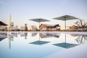 A pool with umbrellas, wooden buildings, and a clear sky. - CALASOLE (Montalto di Castro)